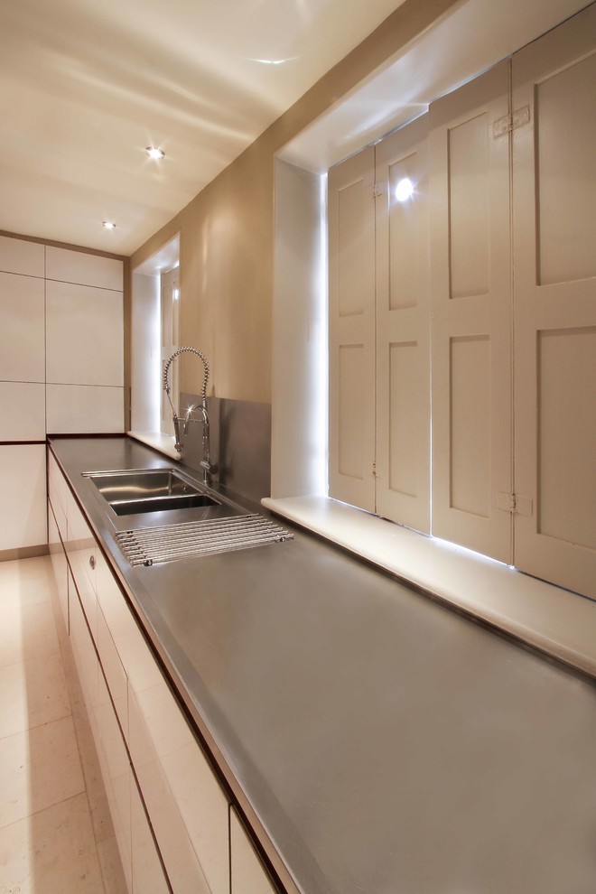 Example of a large danish kitchen design in Hertfordshire with a double-bowl sink, flat-panel cabinets, white cabinets, stainless steel countertops, metallic backsplash, metal backsplash and an island