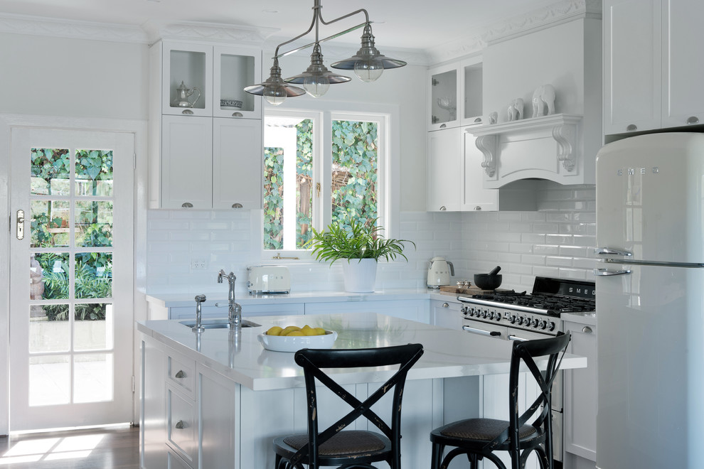 Imagen de cocina clásica de tamaño medio con puertas de armario blancas, salpicadero blanco, salpicadero de azulejos de cerámica, electrodomésticos blancos y una isla