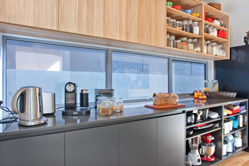 Cette image montre une cuisine design avec des portes de placard noires, un plan de travail en quartz modifié, une crédence en feuille de verre et îlot.