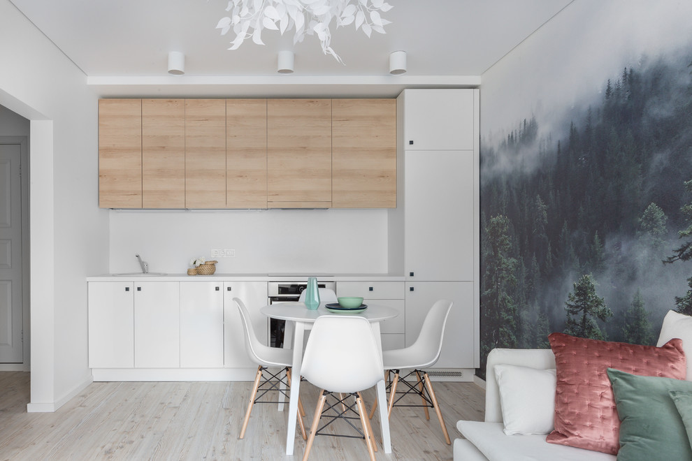 Идея дизайна: прямая кухня-гостиная в скандинавском стиле с плоскими фасадами, фасадами цвета дерева среднего тона, белым фартуком, бежевым полом, светлым паркетным полом, двухцветным гарнитуром и обоями на стенах без острова