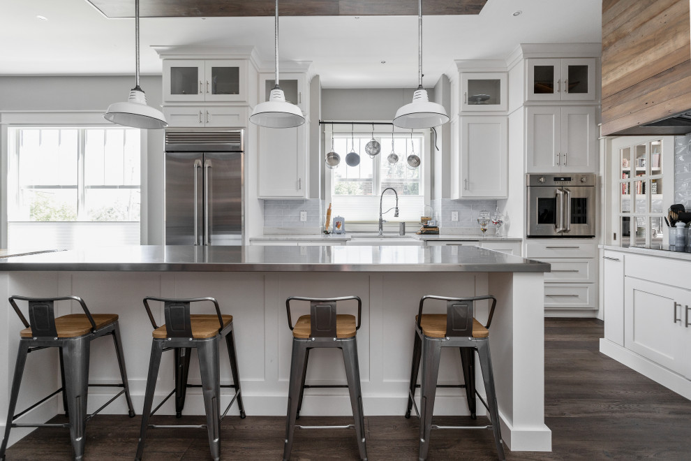 Example of a farmhouse medium tone wood floor and brown floor kitchen design in Indianapolis with shaker cabinets, white cabinets, quartzite countertops, blue backsplash, glass tile backsplash, stainless steel appliances, an island and multicolored countertops