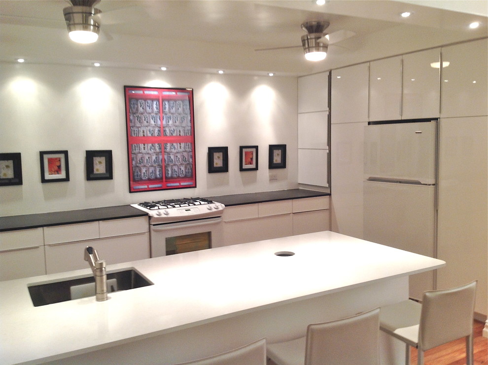 На фото: параллельная кухня среднего размера в современном стиле с врезной мойкой, плоскими фасадами, белыми фасадами, столешницей из кварцита, белой техникой, светлым паркетным полом и полуостровом с