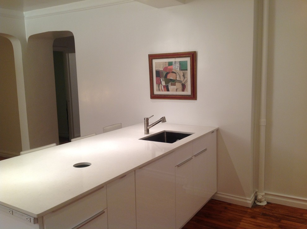 Example of a mid-sized trendy galley light wood floor kitchen design in New York with an undermount sink, flat-panel cabinets, white cabinets, quartzite countertops, white appliances and a peninsula