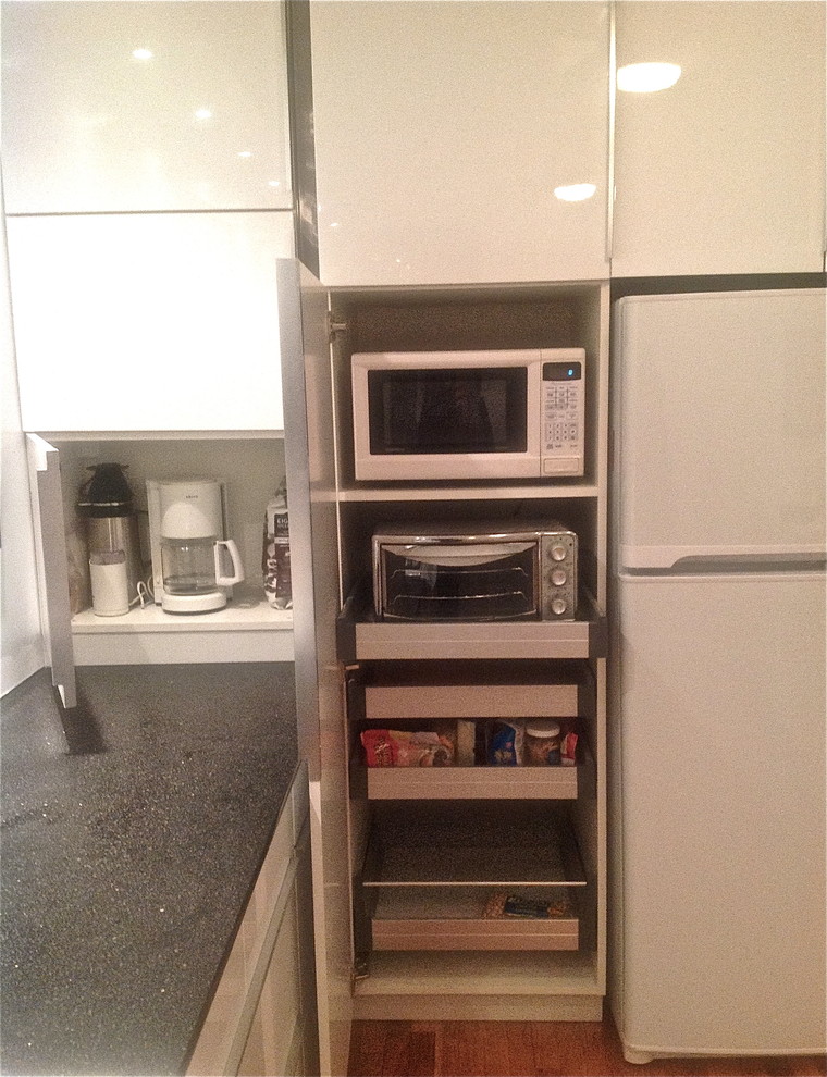This is an example of a medium sized traditional galley kitchen in New York with a submerged sink, flat-panel cabinets, white cabinets, quartz worktops, white appliances, light hardwood flooring and a breakfast bar.