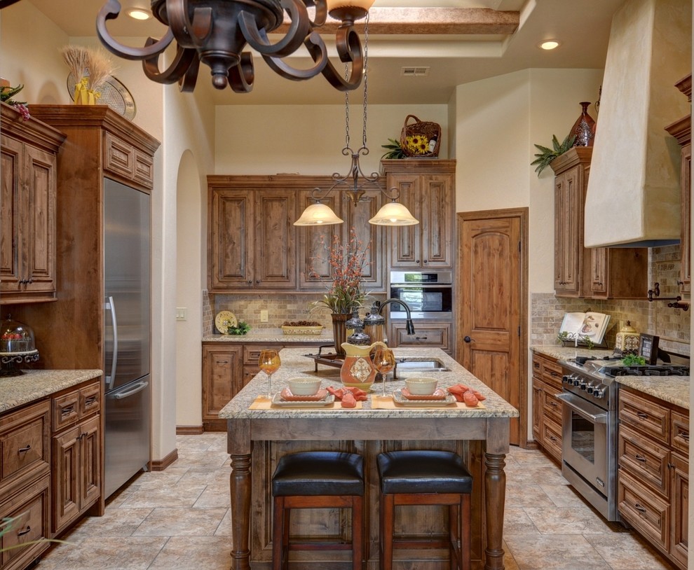 Tuscan porcelain tile eat-in kitchen photo in Austin with an undermount sink, raised-panel cabinets, medium tone wood cabinets, granite countertops, brown backsplash, stone tile backsplash, stainless steel appliances and an island