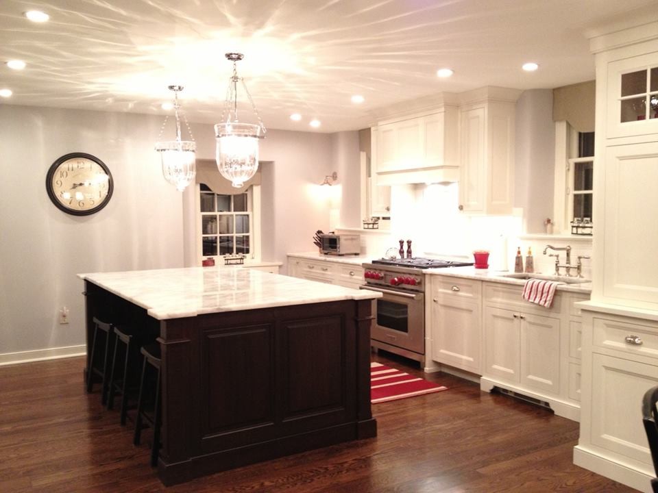Foto på ett stort vintage linjärt kök med öppen planlösning, med en nedsänkt diskho, vita skåp, granitbänkskiva, vitt stänkskydd, rostfria vitvaror, mörkt trägolv och en köksö