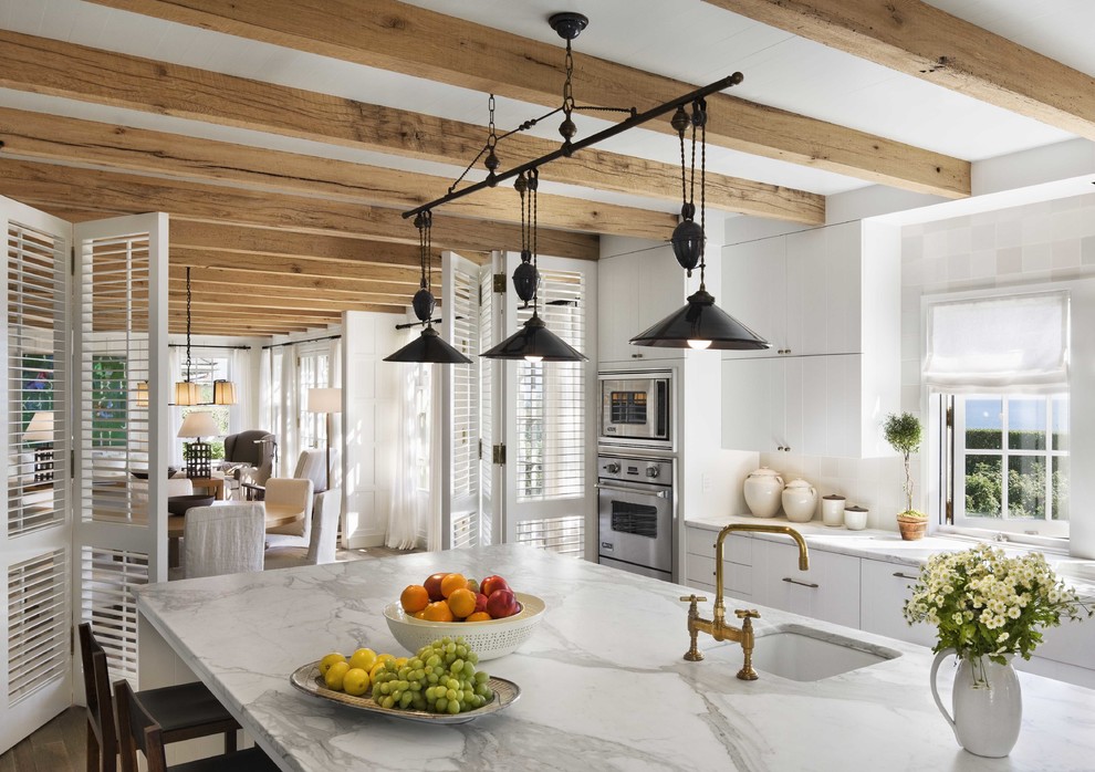 Example of a mid-sized beach style l-shaped dark wood floor enclosed kitchen design in Boston with a farmhouse sink, flat-panel cabinets, white cabinets, marble countertops, white backsplash, ceramic backsplash, stainless steel appliances and an island