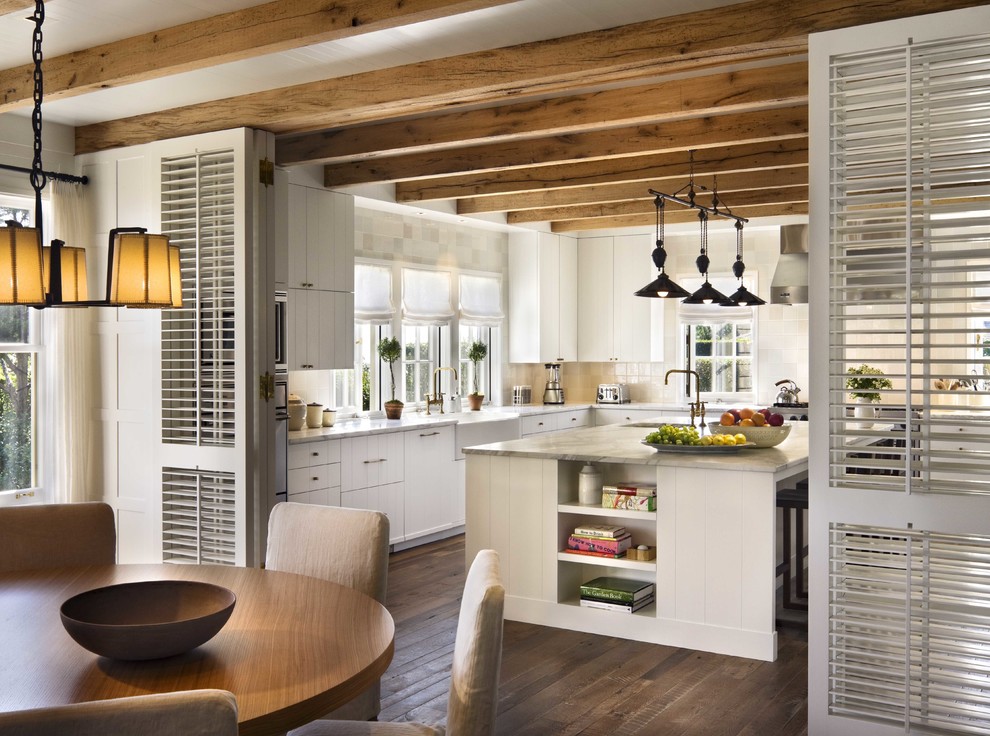 Inspiration for a mid-sized coastal l-shaped dark wood floor enclosed kitchen remodel in Boston with an island, a farmhouse sink, white cabinets, flat-panel cabinets, marble countertops, white backsplash, ceramic backsplash and stainless steel appliances