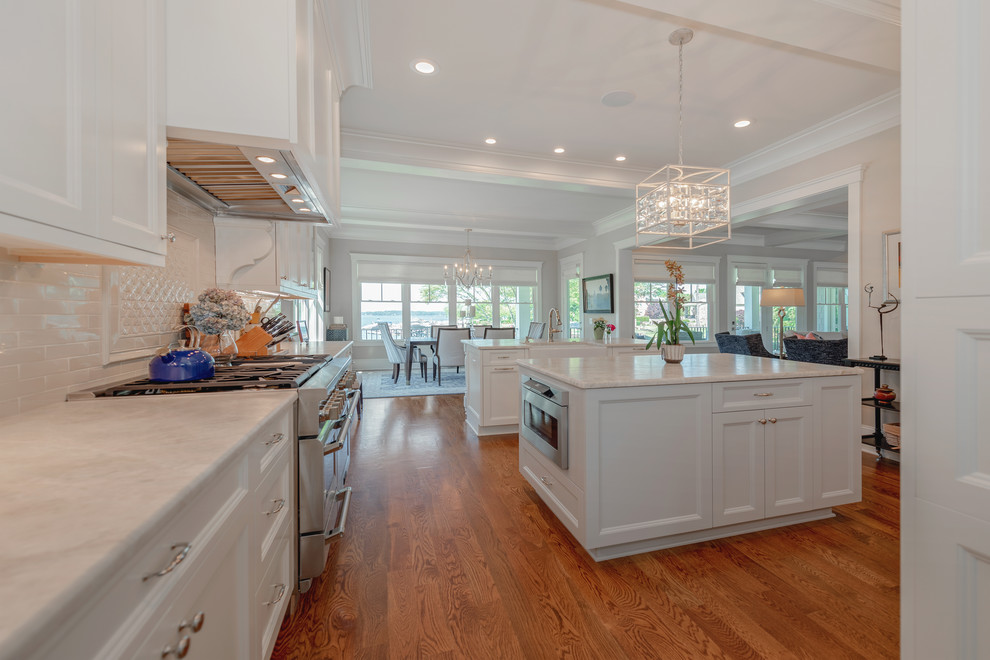 Large beach style u-shaped medium tone wood floor and brown floor eat-in kitchen photo in Charlotte with a farmhouse sink, shaker cabinets, white cabinets, quartz countertops, white backsplash, subway tile backsplash, stainless steel appliances, two islands and white countertops