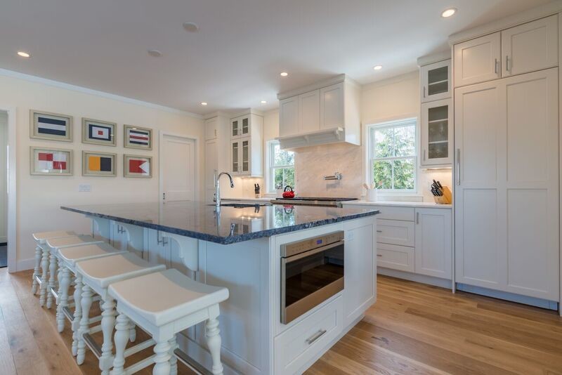 This is an example of a large nautical u-shaped kitchen pantry in Baltimore with flat-panel cabinets, white cabinets, granite worktops, white splashback, stainless steel appliances, light hardwood flooring and an island.