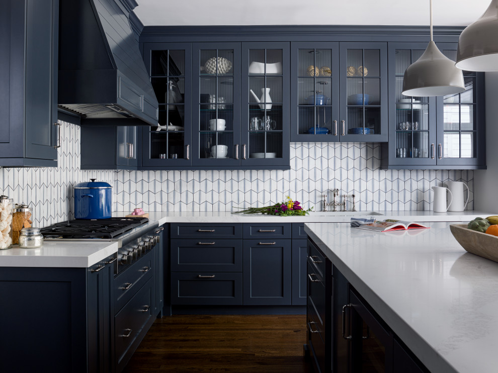 Inredning av ett klassiskt vit vitt l-kök, med en undermonterad diskho, skåp i shakerstil, blå skåp, vitt stänkskydd, rostfria vitvaror, mörkt trägolv, en köksö och brunt golv