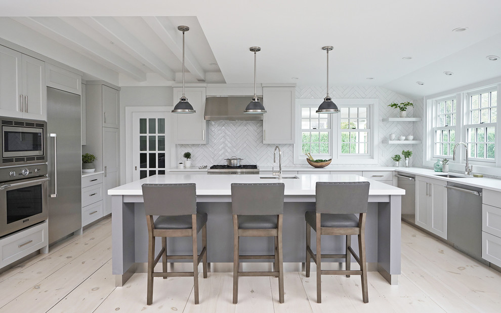 Example of a transitional light wood floor kitchen design with an undermount sink, quartz countertops, white backsplash, ceramic backsplash, stainless steel appliances, an island, white countertops, shaker cabinets and gray cabinets