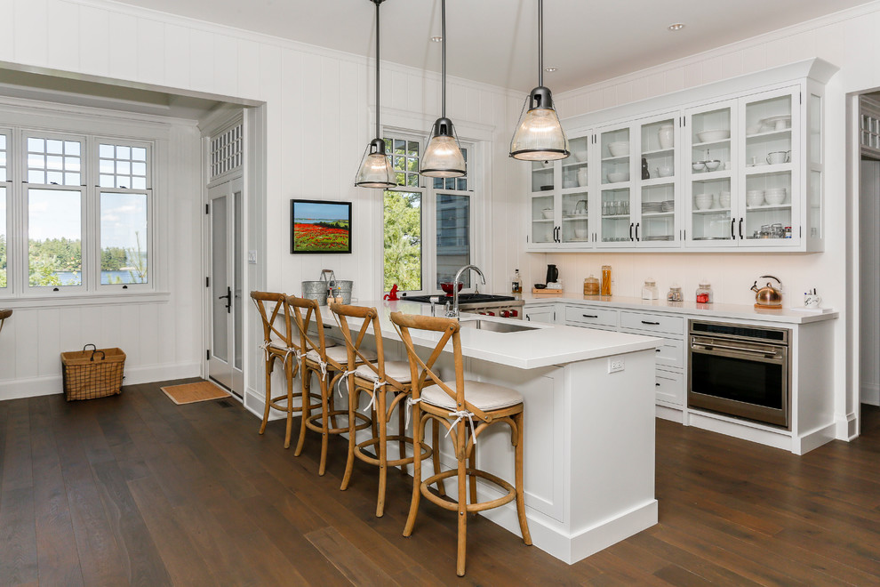 Photo of a nautical kitchen in Toronto with a submerged sink, glass-front cabinets, white cabinets, stainless steel appliances, dark hardwood flooring and a breakfast bar.