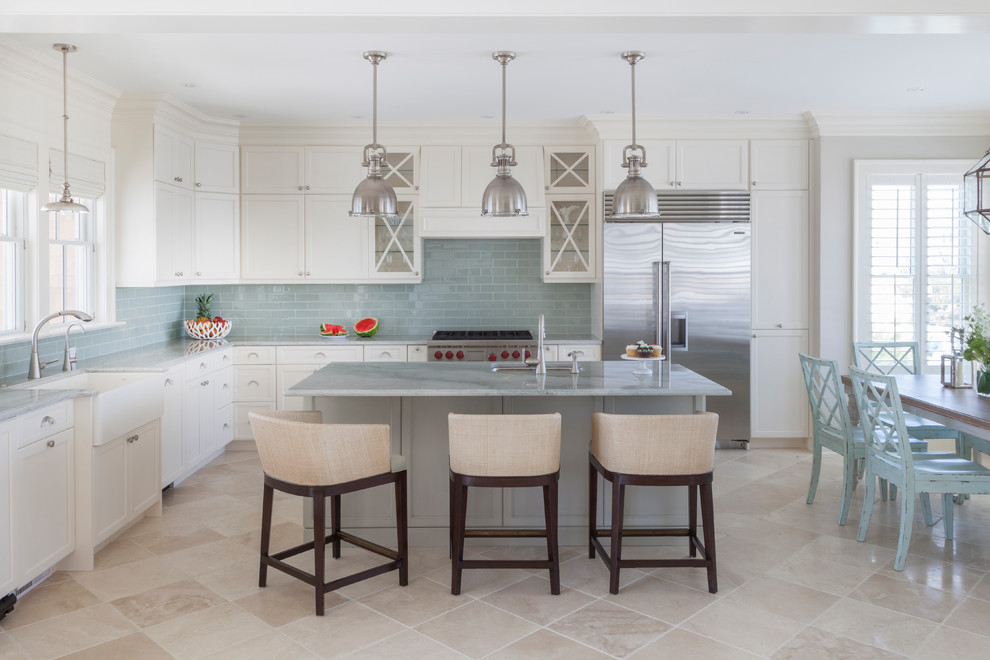 Inspiration for a beach style l-shaped kitchen/diner in New York with a belfast sink, shaker cabinets, white cabinets, blue splashback, metro tiled splashback, stainless steel appliances, an island, beige floors and travertine flooring.
