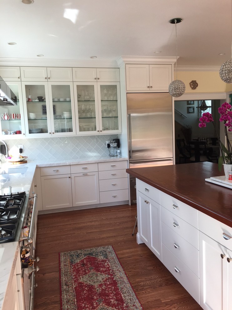 Medium sized classic l-shaped enclosed kitchen in San Francisco with shaker cabinets, white cabinets, stainless steel appliances, medium hardwood flooring, an island, brown floors, engineered stone countertops, white splashback, glass tiled splashback and white worktops.
