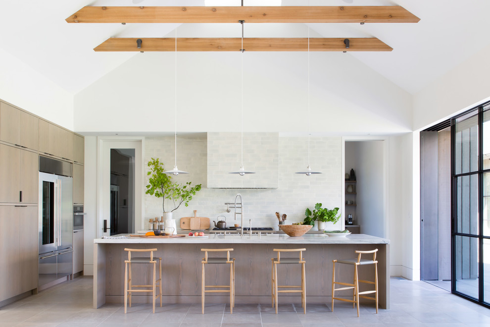 This is an example of a country l-shaped kitchen in San Francisco with a submerged sink, flat-panel cabinets, light wood cabinets, white splashback, metro tiled splashback, stainless steel appliances, an island, grey floors and white worktops.