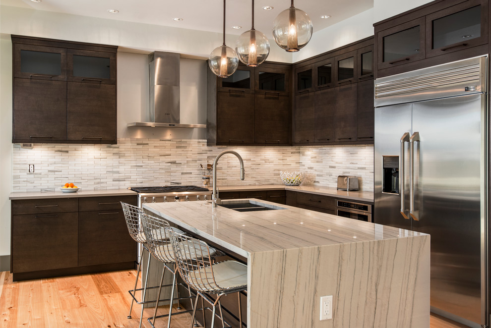 Mid-sized transitional l-shaped light wood floor and brown floor open concept kitchen photo in Miami with a double-bowl sink, flat-panel cabinets, dark wood cabinets, beige backsplash, matchstick tile backsplash, stainless steel appliances, an island and quartz countertops