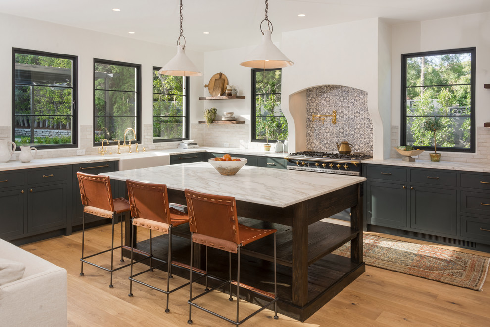 Mediterranean l-shaped kitchen in Los Angeles with shaker cabinets, an island, a belfast sink, multi-coloured splashback, black appliances, light hardwood flooring, multicoloured worktops and green cabinets.