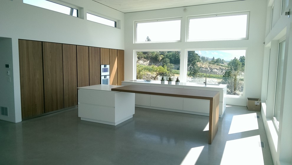 This is an example of a large contemporary u-shaped open plan kitchen in Vancouver with a submerged sink, flat-panel cabinets, medium wood cabinets, stainless steel appliances, concrete flooring and multiple islands.