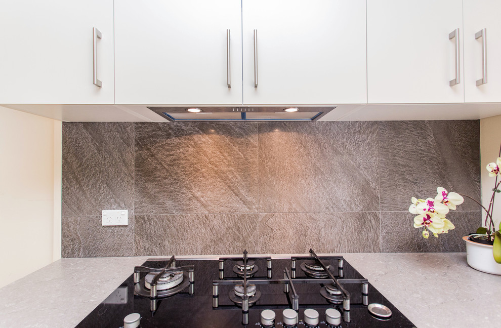 This is an example of a medium sized contemporary u-shaped kitchen/diner in Other with a built-in sink, flat-panel cabinets, white cabinets, laminate countertops, grey splashback, ceramic splashback, stainless steel appliances, ceramic flooring, a breakfast bar, brown floors and grey worktops.