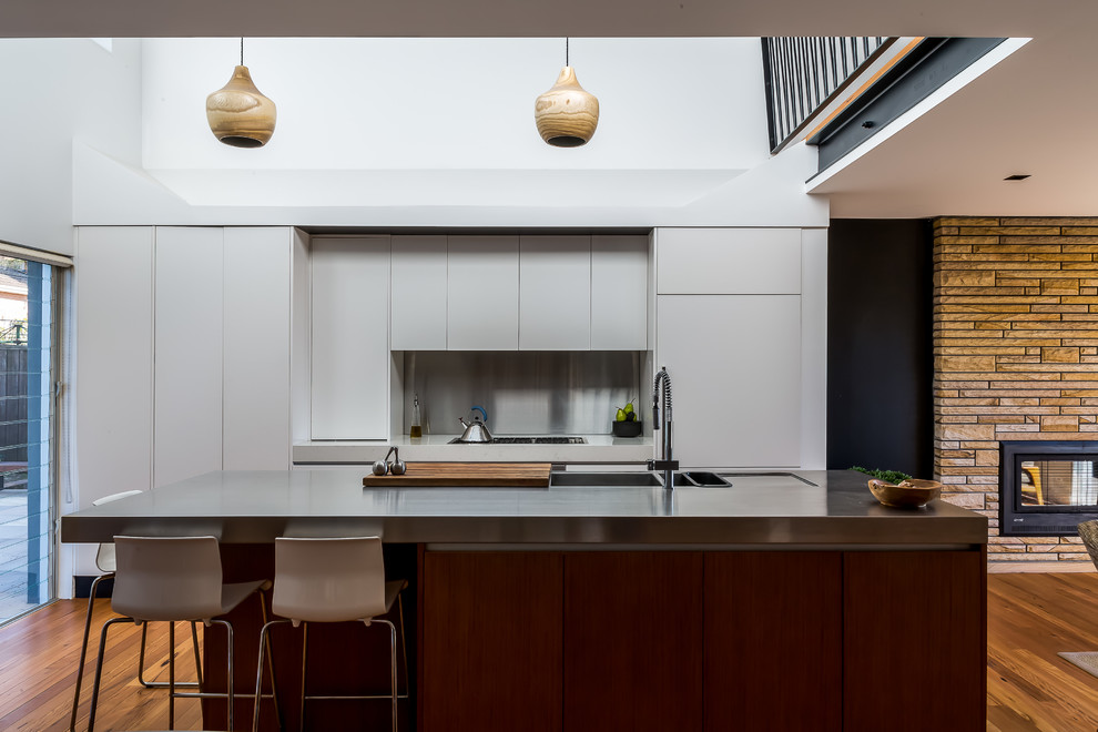 Zweizeilige Moderne Küche mit flächenbündigen Schrankfronten, weißen Schränken, Edelstahl-Arbeitsplatte, braunem Holzboden, Kücheninsel, grauem Boden und grauer Arbeitsplatte in Sonstige