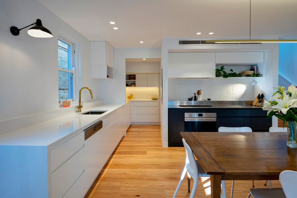 Moderne Küche mit Unterbauwaschbecken, Edelstahl-Arbeitsplatte, Küchenrückwand in Weiß, Rückwand aus Keramikfliesen, Küchengeräten aus Edelstahl, braunem Holzboden und weißer Arbeitsplatte in Sydney