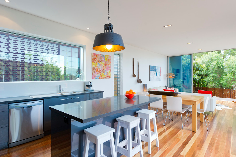 Ejemplo de cocinas en L minimalista de tamaño medio con salpicadero blanco, electrodomésticos de acero inoxidable, suelo de madera en tonos medios y una isla