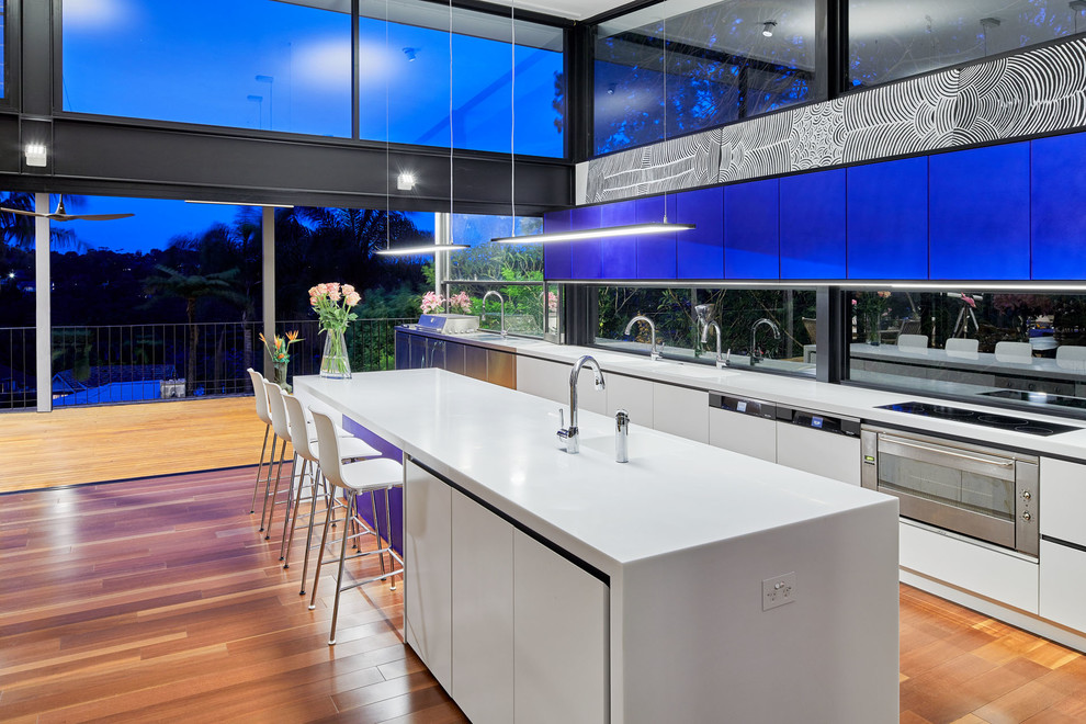 Immagine di una grande cucina moderna con lavello a doppia vasca, ante lisce, ante blu, top in superficie solida, elettrodomestici da incasso, pavimento in legno massello medio e pavimento marrone