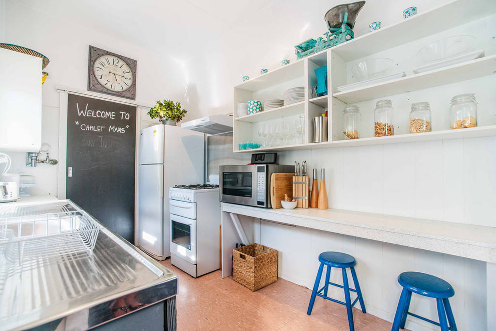 Diseño de cocina costera pequeña con puertas de armario grises, encimera de laminado, salpicadero blanco, electrodomésticos blancos y suelo de linóleo