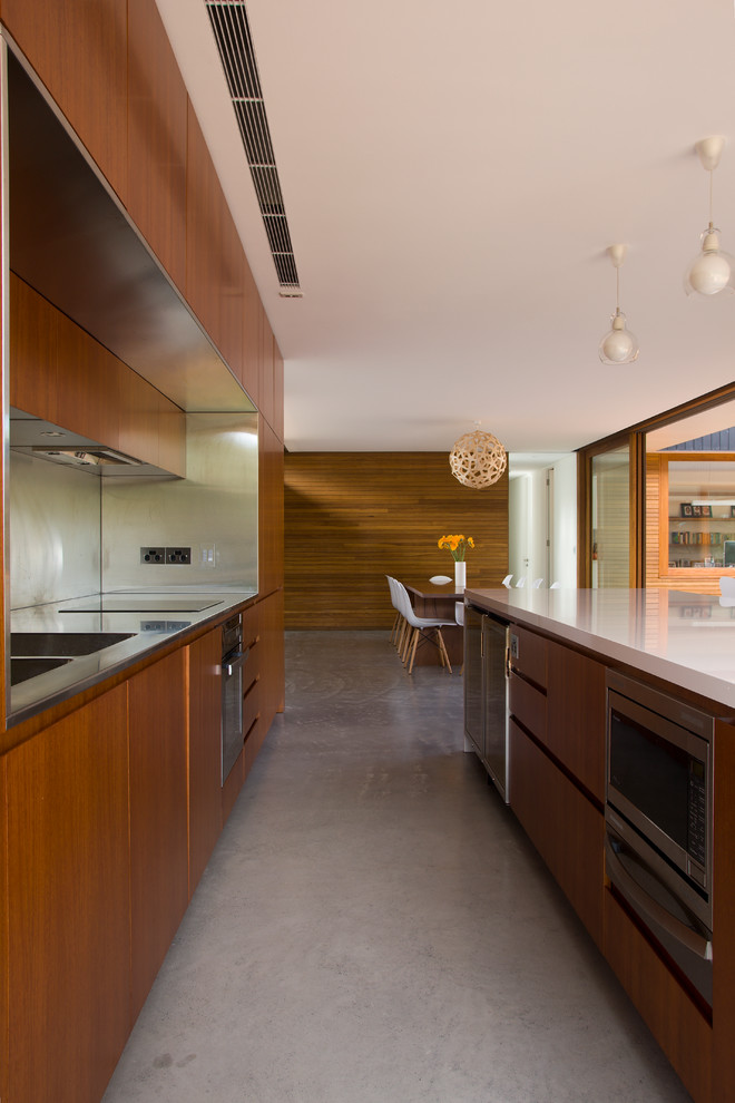 Immagine di una cucina minimalista di medie dimensioni con ante lisce, ante in legno bruno, paraspruzzi a effetto metallico, elettrodomestici in acciaio inossidabile, pavimento in cemento, pavimento grigio e top bianco