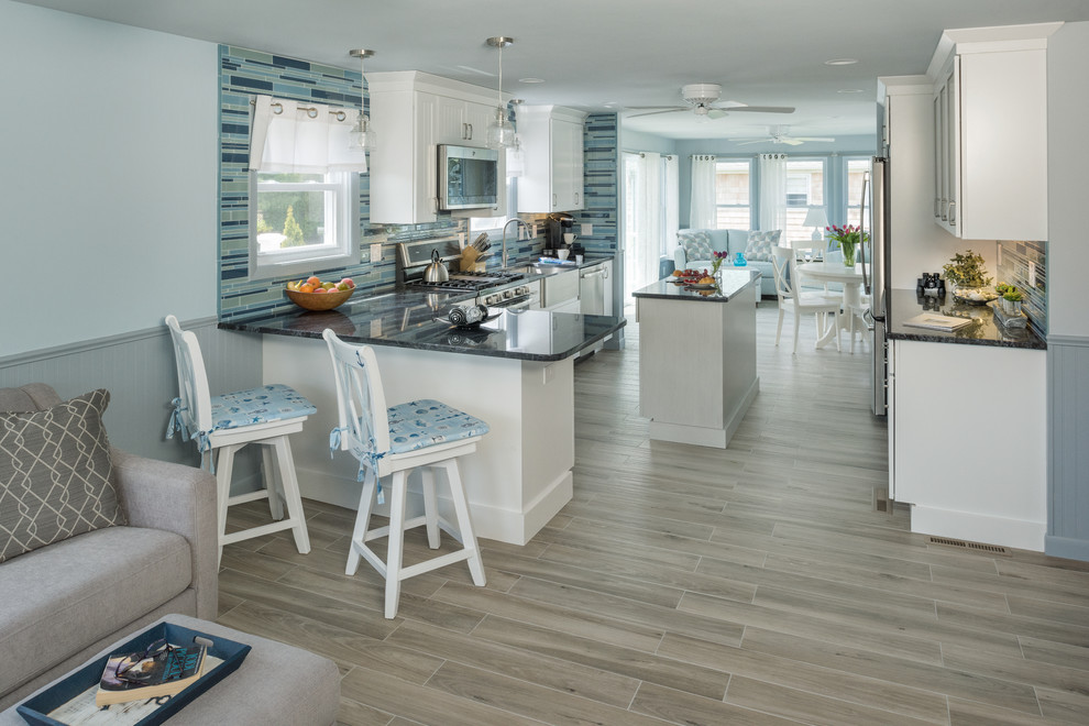 Eat-in kitchen - small coastal galley porcelain tile and gray floor eat-in kitchen idea in Providence with a farmhouse sink, recessed-panel cabinets, white cabinets, granite countertops, blue backsplash, glass tile backsplash, stainless steel appliances and an island