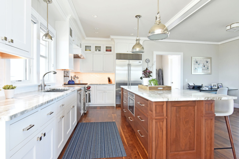 Design ideas for a large classic l-shaped open plan kitchen in Providence with a double-bowl sink, recessed-panel cabinets, white cabinets, marble worktops, white splashback, metro tiled splashback, stainless steel appliances, medium hardwood flooring, an island, brown floors and white worktops.