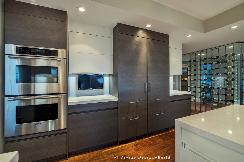 Contemporary kitchen/diner in Boston with a submerged sink, flat-panel cabinets, grey cabinets, white splashback, glass sheet splashback, stainless steel appliances, medium hardwood flooring and an island.