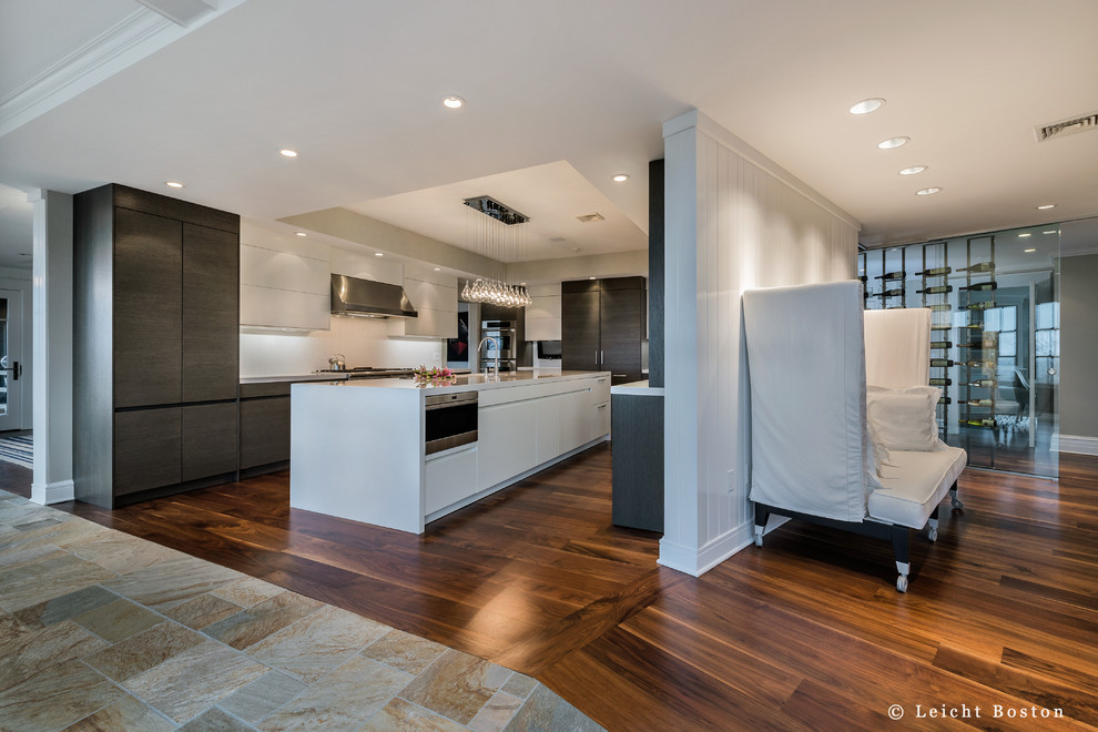 Photo of an expansive contemporary u-shaped kitchen pantry in Boston with a submerged sink, flat-panel cabinets, dark wood cabinets, engineered stone countertops, white splashback, glass sheet splashback, white appliances, dark hardwood flooring and an island.