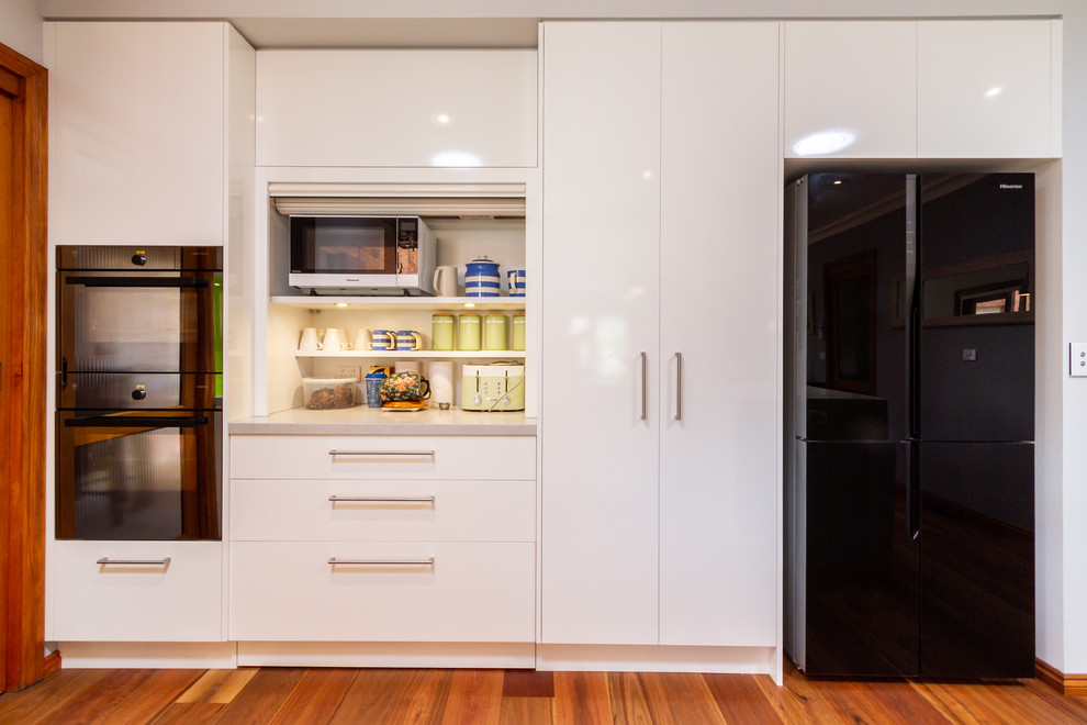 Photo of a medium sized contemporary u-shaped kitchen/diner in Melbourne with a submerged sink, flat-panel cabinets, white cabinets, engineered stone countertops, green splashback, glass sheet splashback, black appliances, medium hardwood flooring, a breakfast bar, brown floors and white worktops.