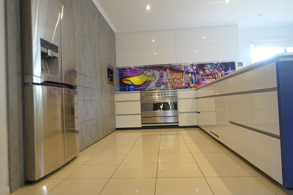 This is an example of a large contemporary l-shaped open plan kitchen in Melbourne with a double-bowl sink, flat-panel cabinets, white cabinets, engineered stone countertops, multi-coloured splashback, glass sheet splashback, stainless steel appliances, porcelain flooring, an island and beige floors.