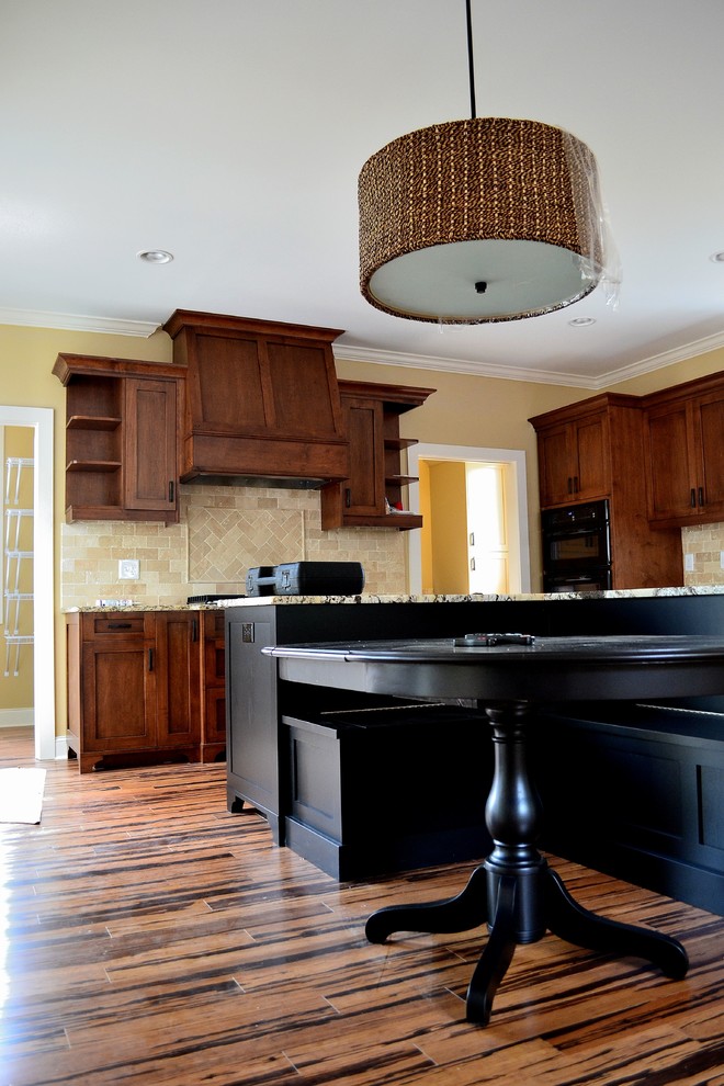Immagine di una cucina eclettica di medie dimensioni con lavello sottopiano, ante lisce, ante in legno bruno, top in granito, paraspruzzi beige, elettrodomestici neri e pavimento in bambù