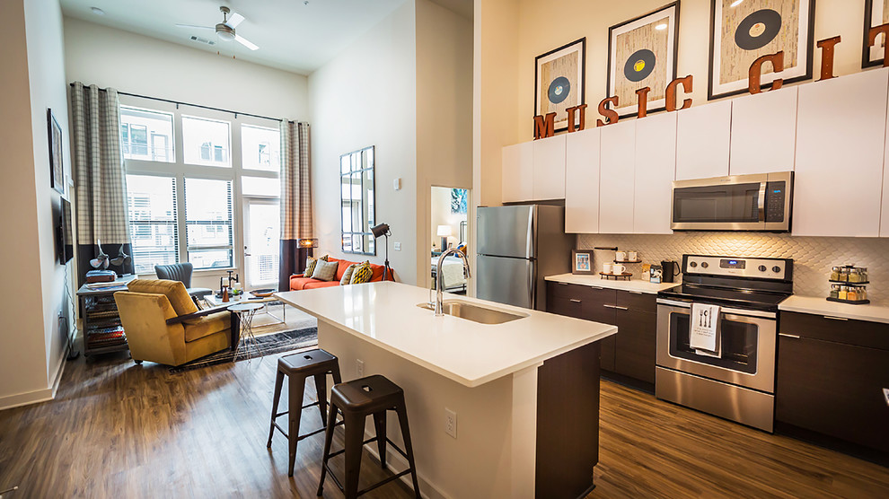 Medium sized modern l-shaped open plan kitchen in Miami with a submerged sink, flat-panel cabinets, white cabinets, engineered stone countertops, white splashback, porcelain splashback, stainless steel appliances, vinyl flooring, an island and brown floors.