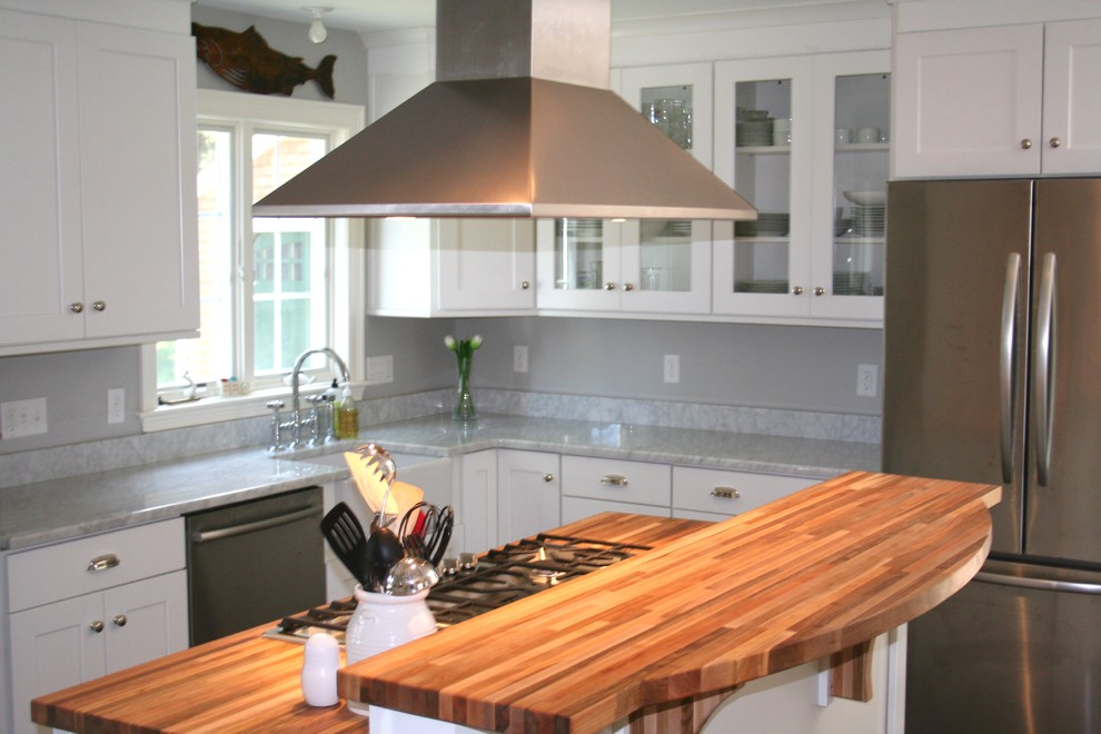 Inspiration for a mid-sized timeless single-wall medium tone wood floor kitchen pantry remodel in Providence with an island, shaker cabinets, white cabinets, marble countertops, gray backsplash, stainless steel appliances and a farmhouse sink