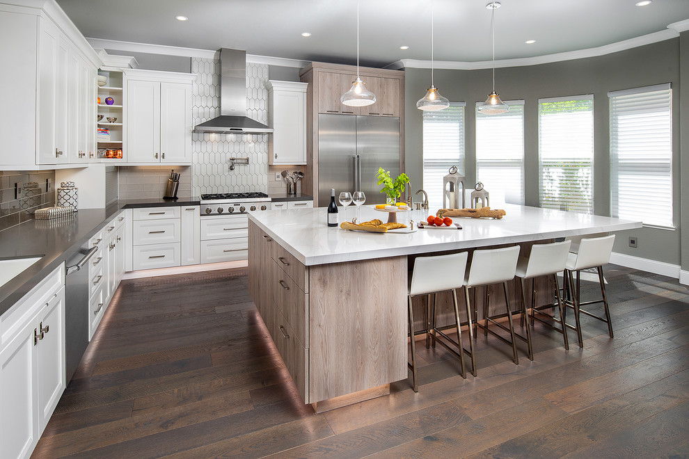 Kitchen - large transitional l-shaped brown floor and dark wood floor kitchen idea in Sacramento with a single-bowl sink, white cabinets, quartz countertops, gray backsplash, glass tile backsplash, stainless steel appliances, an island, white countertops and recessed-panel cabinets