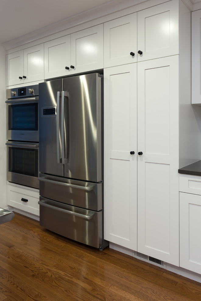 Modern inredning av ett mellanstort kök, med en undermonterad diskho, skåp i shakerstil, vita skåp, marmorbänkskiva, vitt stänkskydd, stänkskydd i marmor, rostfria vitvaror, mellanmörkt trägolv och en köksö