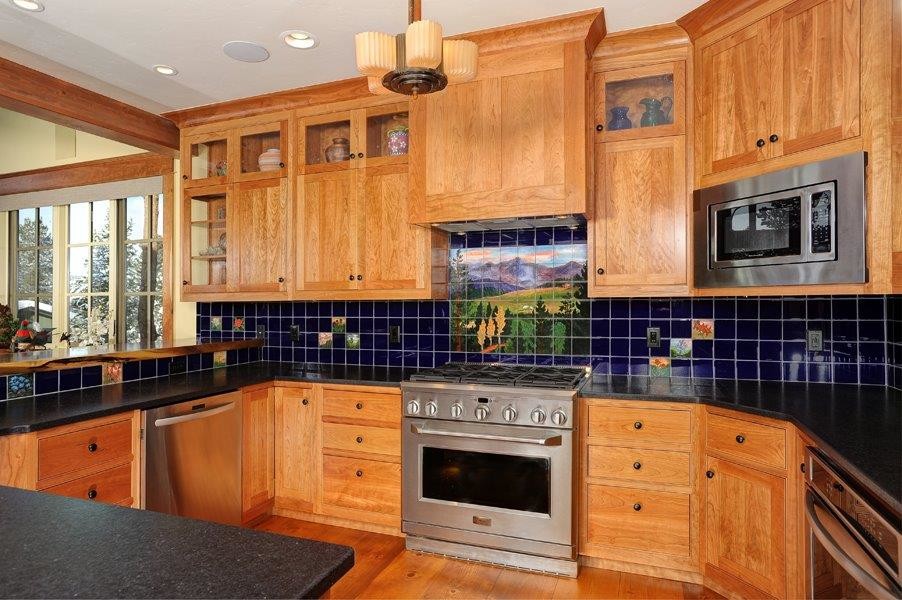 Example of an arts and crafts u-shaped medium tone wood floor eat-in kitchen design in Denver with a drop-in sink, flat-panel cabinets, medium tone wood cabinets, limestone countertops, black backsplash, glass tile backsplash, stainless steel appliances and an island
