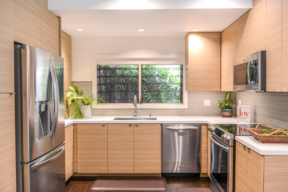 Cette image montre une cuisine design en U et bois clair avec un évier encastré, un placard à porte plane, une crédence grise, un électroménager en acier inoxydable et aucun îlot.
