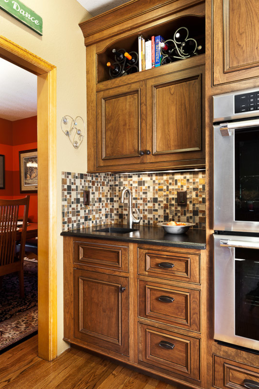 Klassisk inredning av ett stort kök, med en undermonterad diskho, granitbänkskiva, flerfärgad stänkskydd, stänkskydd i glaskakel, rostfria vitvaror, luckor med upphöjd panel, bruna skåp, ljust trägolv och flera köksöar