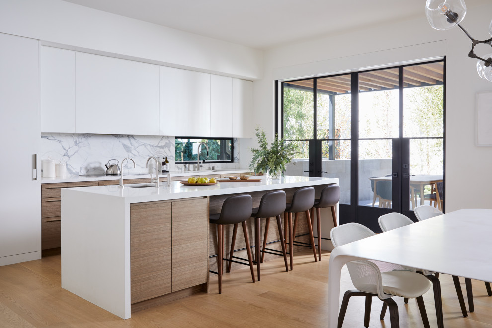 Photo of a modern galley kitchen in San Francisco with flat-panel cabinets, white cabinets, white splashback, integrated appliances, medium hardwood flooring, an island, brown floors and white worktops.