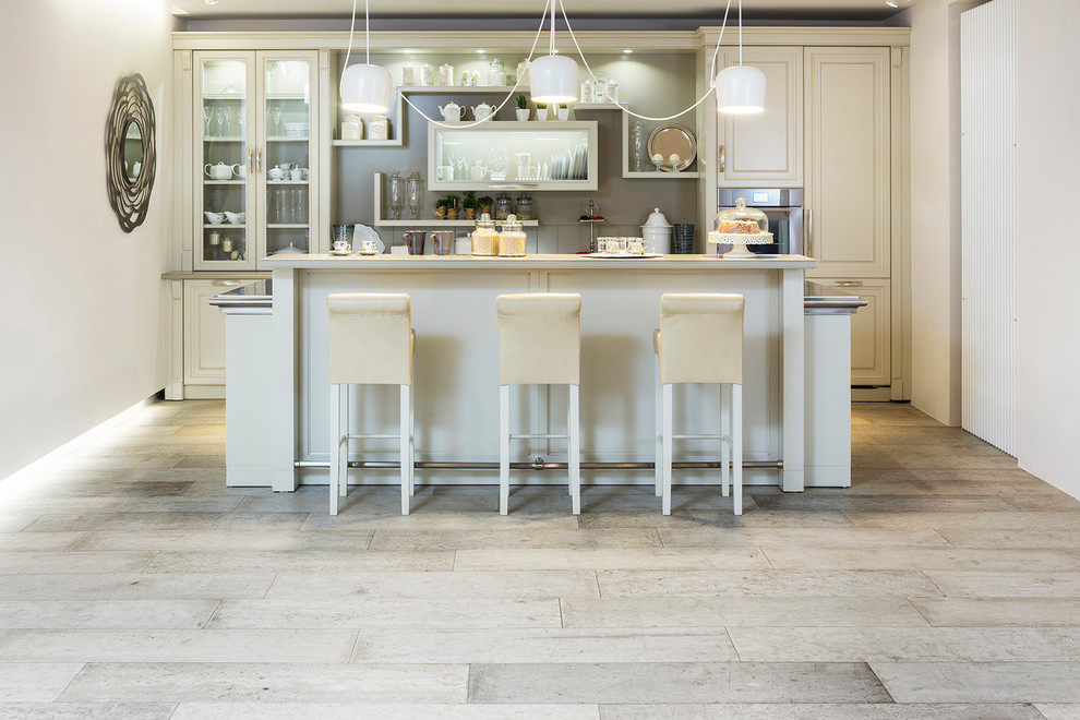 Rustic kitchen with beige cabinets, beige splashback, glass tiled splashback, stainless steel appliances, concrete flooring, an island and grey floors.
