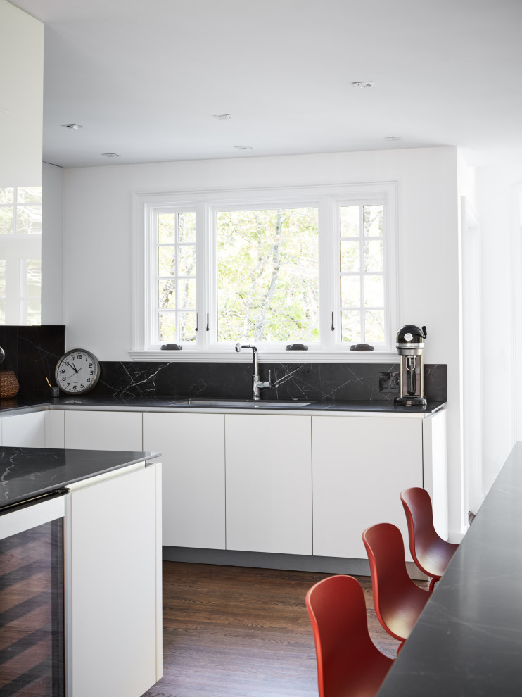 Idee per una grande cucina minimalista con lavello sottopiano, ante di vetro, ante bianche, paraspruzzi nero, elettrodomestici in acciaio inossidabile, parquet scuro, pavimento marrone e top nero