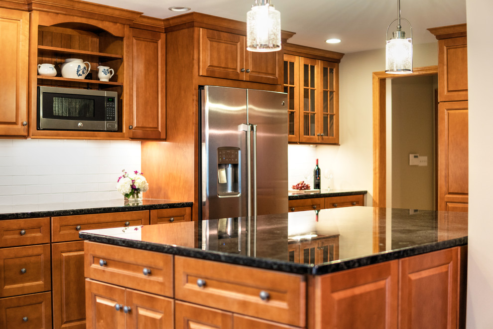 Bild på ett stort vintage kök, med en undermonterad diskho, luckor med upphöjd panel, skåp i mellenmörkt trä, granitbänkskiva, vitt stänkskydd, stänkskydd i keramik, rostfria vitvaror, klinkergolv i keramik, en köksö och grått golv