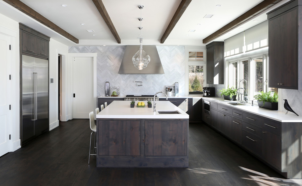 This is an example of an expansive contemporary l-shaped kitchen/diner in New York with a belfast sink, recessed-panel cabinets, dark wood cabinets, engineered stone countertops, white splashback, marble splashback, stainless steel appliances, dark hardwood flooring and an island.