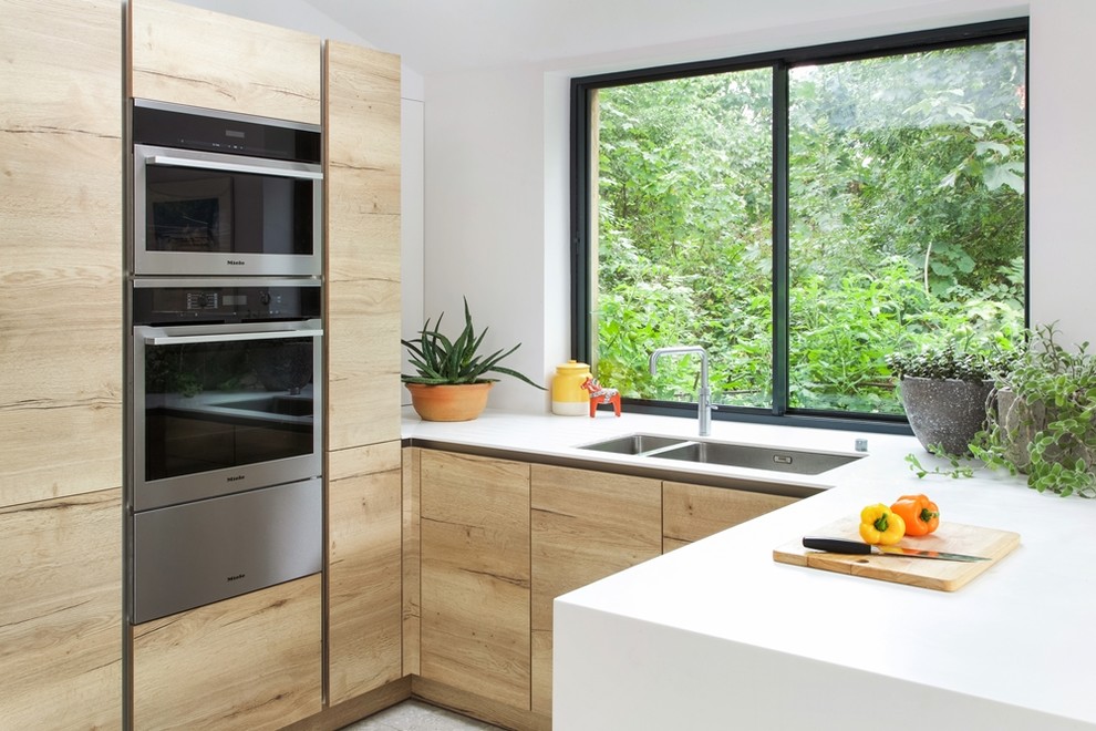 Inspiration for a medium sized contemporary l-shaped kitchen/diner in London with an integrated sink, flat-panel cabinets, light wood cabinets, composite countertops, white splashback, window splashback, stainless steel appliances, concrete flooring, no island and grey floors.